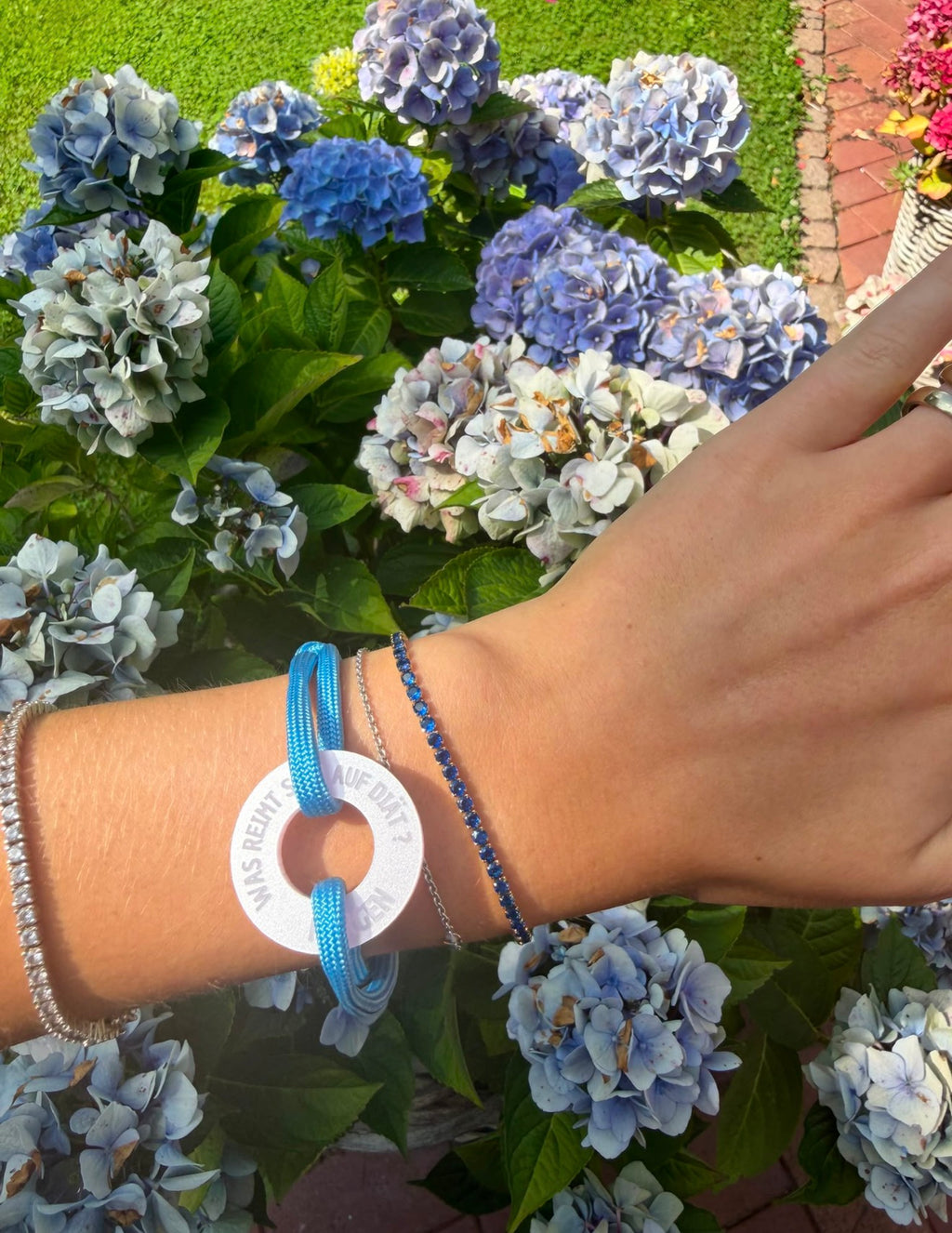 Saphirblaues Zirkonia-Tennisarmband kombiniert mit einem Happycoin Armband am Handgelenk