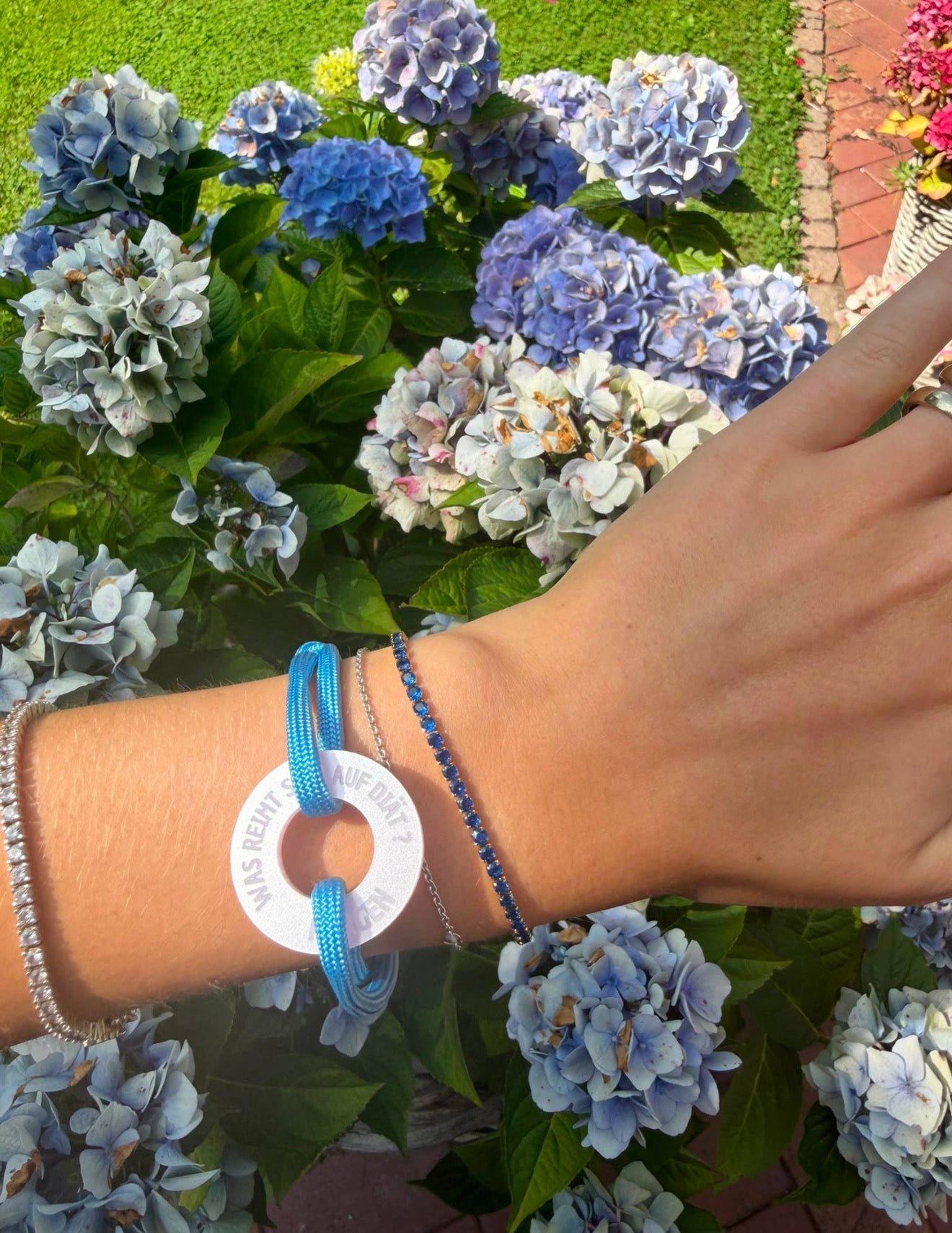 Saphirblaues Zirkonia-Tennisarmband kombiniert mit einem Happycoin Armband am Handgelenk