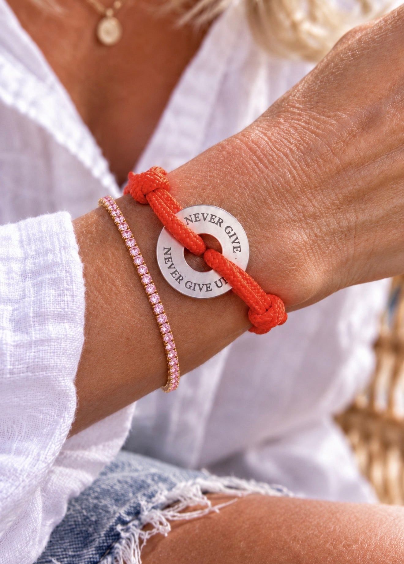 Rosafarbenes Zirkonia-Tennisarmband kombiniert mit einem Happycoin "Never give up" Armband am Handgelenk