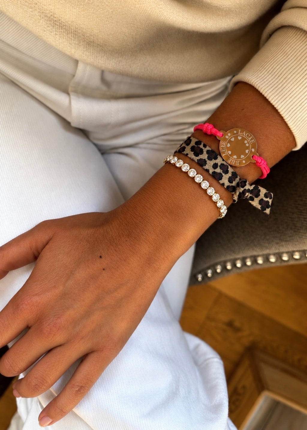 Happycoin-Armband in Pink mit goldfarbenem Coin und Leo-Armband am Handgelenk, kombiniert mit einem zusätzlichen Tennisarmband.“
